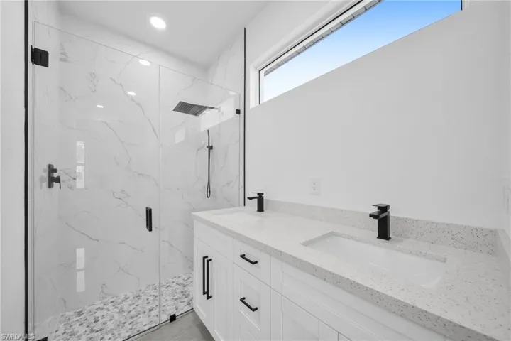 Full bath featuring a marble finish shower, double vanity, and recessed lighting