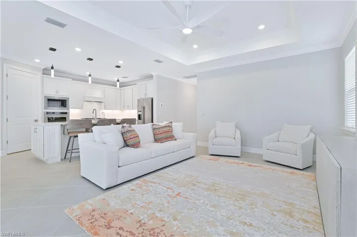 Living room featuring crown molding, recessed lighting, ceiling fan, light tile patterned floors, and a raised ceiling