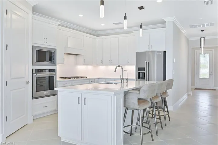 Kitchen with pendant lighting, appliances with stainless steel finishes, ornamental molding, white cabinets, and a kitchen bar