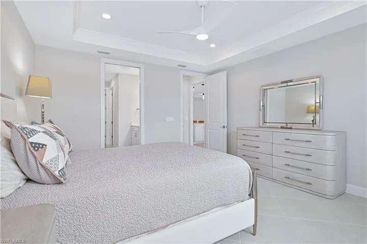 Bedroom with ornamental molding, a raised ceiling, recessed lighting, a ceiling fan, and ensuite bath