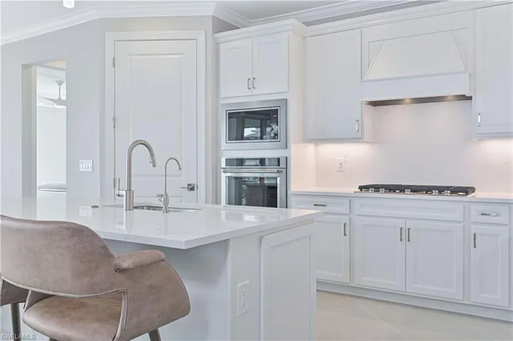 Kitchen with premium range hood, white cabinetry, appliances with stainless steel finishes, light stone counters, and crown molding