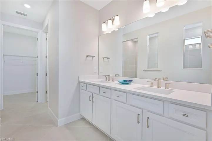 Bathroom with a walk in closet, double vanity, and light tile patterned floors