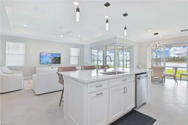 Kitchen featuring pendant lighting, open floor plan, a kitchen bar, white cabinetry, and light stone countertops