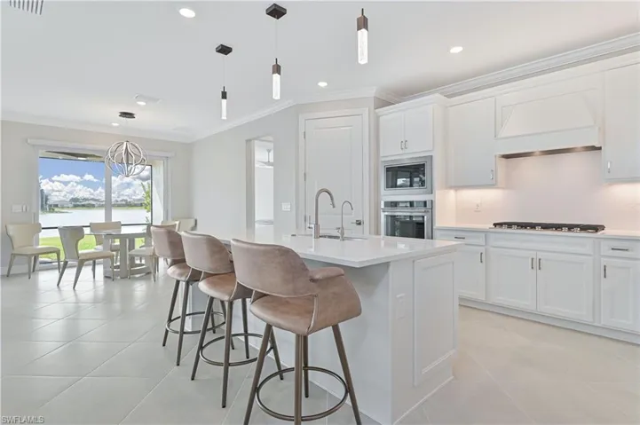 Kitchen with hanging light fixtures, ornamental molding, white cabinets, custom exhaust hood, and stainless steel appliances