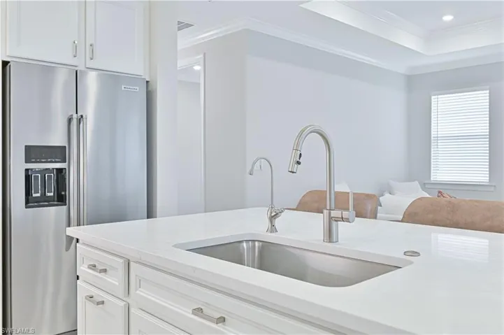 Kitchen featuring white cabinets, crown molding, high end fridge, light stone counters, and a raised ceiling