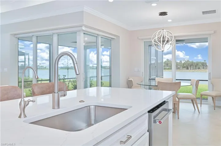 Kitchen featuring light stone counters, pendant lighting, a water view, crown molding, and white cabinets