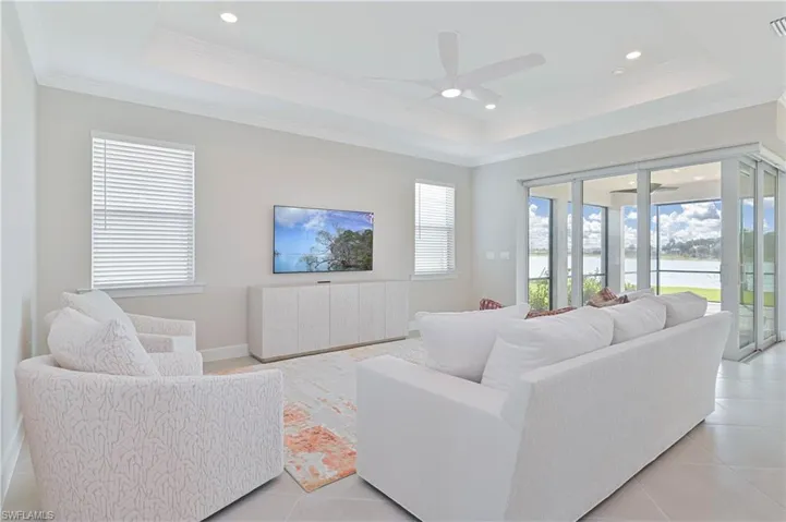 Living area with a ceiling fan, light tile patterned flooring, a raised ceiling, ornamental molding, and recessed lighting