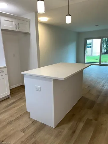 Kitchen with light wood finished floors, white cabinets, decorative light fixtures, and light countertops