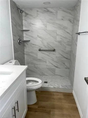 Full bathroom featuring vanity, a marble finish shower, and wood finished floors
