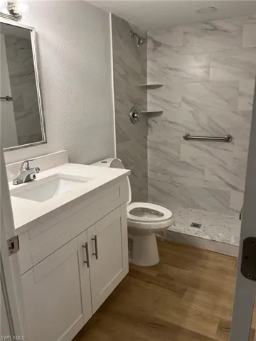 Bathroom with vanity, a marble finish shower, wood finished floors, and a textured wall