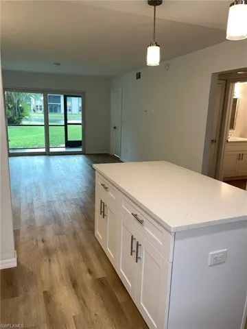 Kitchen with wood finished floors, a center island, white cabinetry, hanging light fixtures, and open floor plan