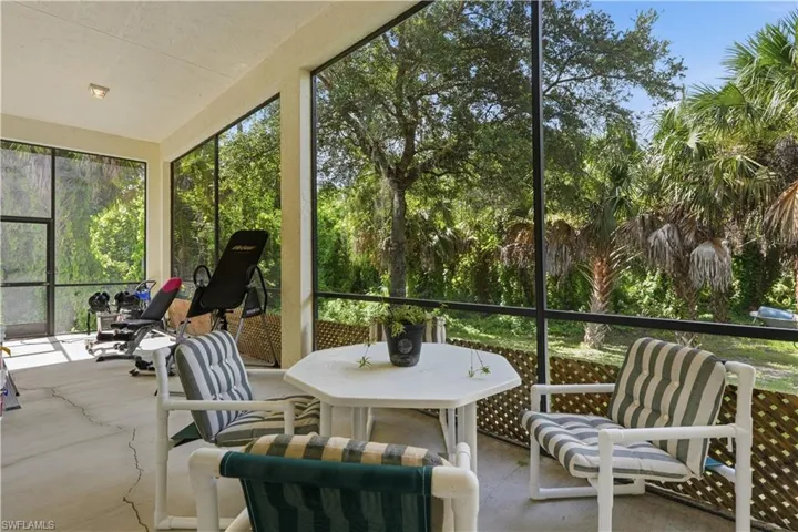 Screened lanai featuring concrete flooring, a textured ceiling, and expansive views of mature trees and tropical foliage