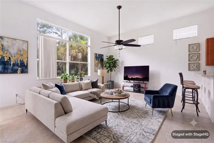 Spacious living area featuring large windows, transom windows, a ceiling fan, tiled flooring, and a breakfast bar with seating. Furnishings virtually Staged