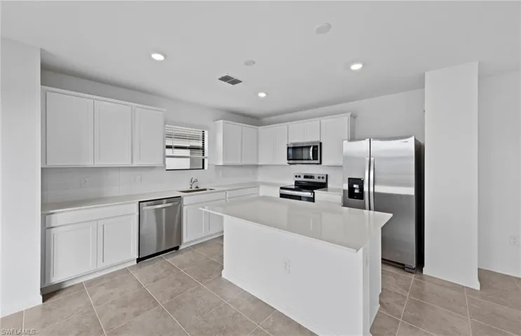 Kitchen with stainless steel appliances, white cabinetry, light tile patterned flooring, a center island, and recessed lighting