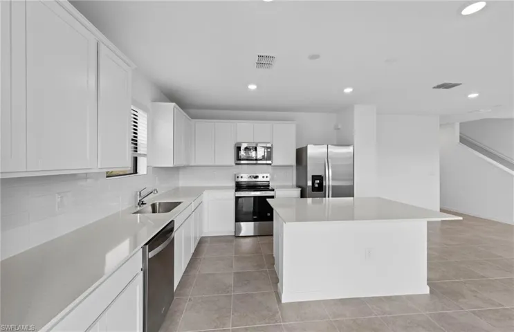 Kitchen featuring stainless steel appliances, a kitchen island, white cabinets, backsplash, and recessed lighting