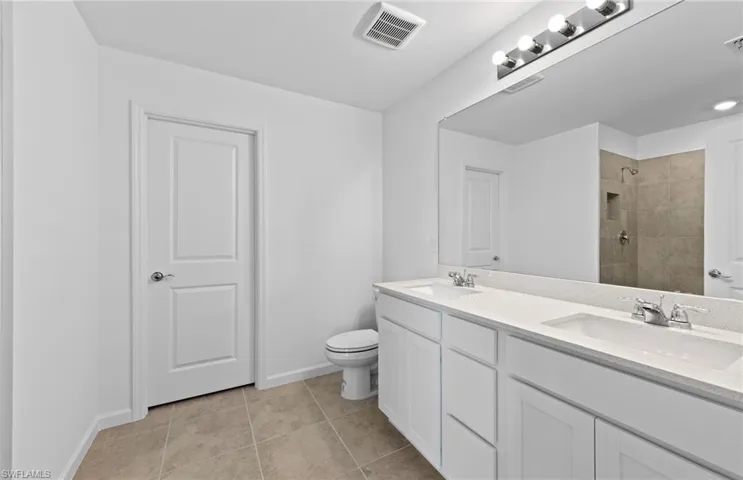 Bathroom with tiled shower, double vanity, and light tile patterned floors