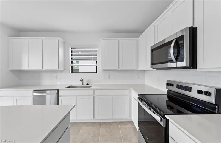 Kitchen with stainless steel appliances, backsplash, white cabinetry, light tile patterned floors, and light stone countertops