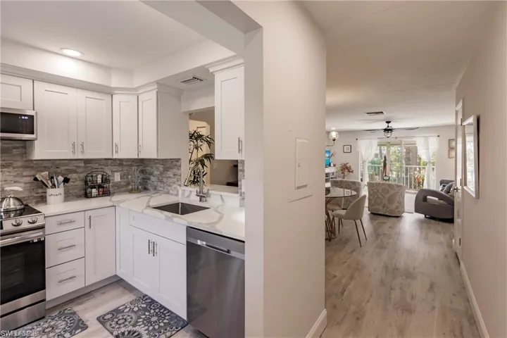 Kitchen with ceiling fan, appliances with stainless steel finishes, a sink, light wood-style flooring, and backsplash