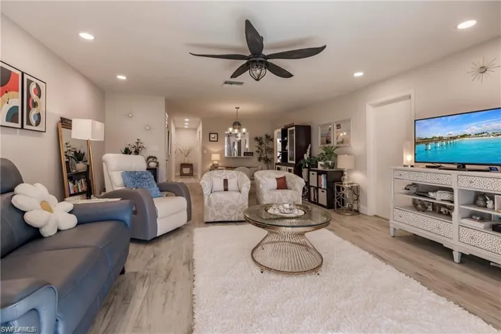 Living area featuring ceiling fan with notable chandelier, recessed lighting, wood finished floors, and visible vents