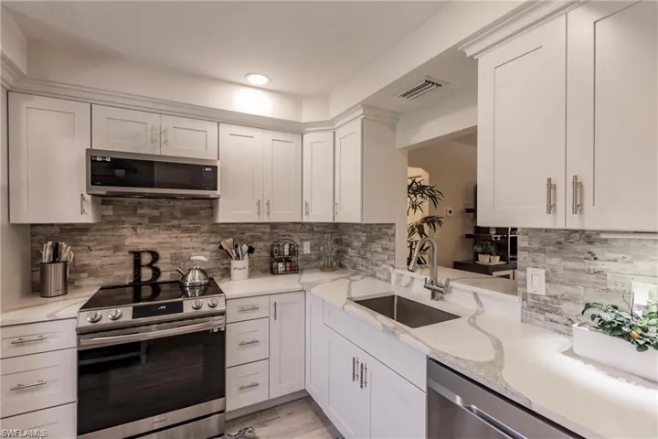 Kitchen with visible vents, decorative backsplash, white cabinets, a sink, and stainless steel appliances