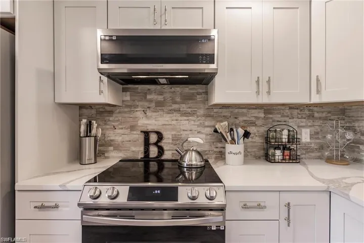 Kitchen with light stone counters, appliances with stainless steel finishes, tasteful backsplash, and white cabinetry