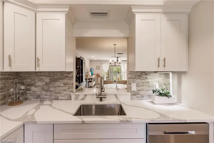 Kitchen with decorative backsplash, visible vents, stainless steel dishwasher, a sink, and white cabinetry