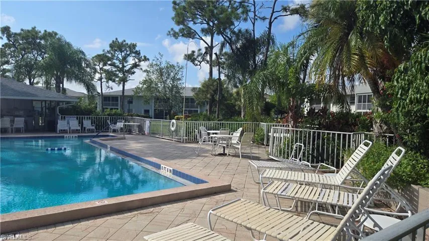 Community pool with a patio area, fence, and outdoor dry bar