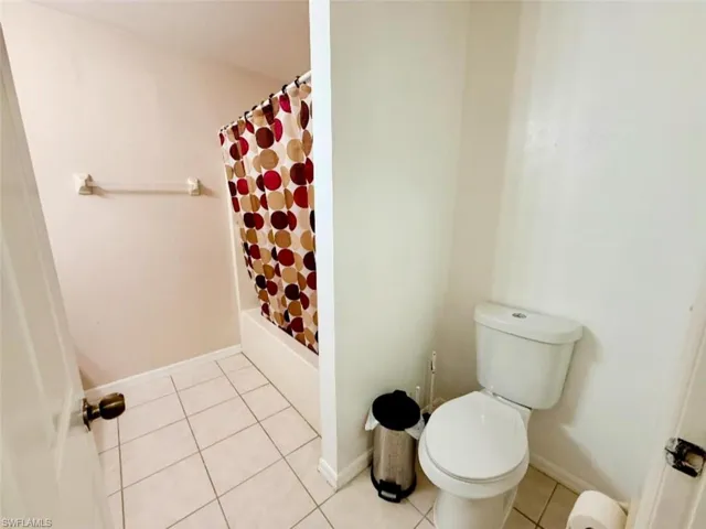 Bathroom featuring tile patterned flooring, toilet, and shower / bathtub combination with curtain