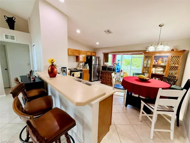 Kitchen with appliances with stainless steel finishes, vaulted ceiling, light tile patterned flooring, a peninsula, and a sink