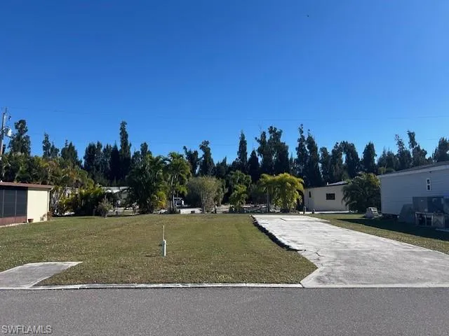View of front of house with a front yard, concrete driveway, and view of wooded area