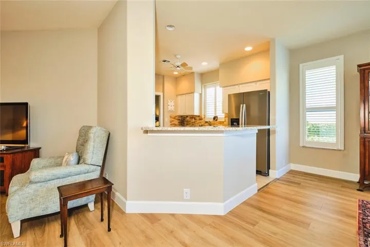 Kitchen featuring stainless steel fridge with ice dispenser, light wood finished floors, white cabinetry, baseboards, and light stone countertops