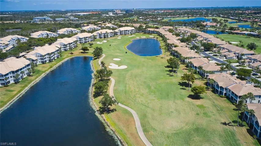 Aerial view of property and surrounding area featuring a nearby body of water, a golf course, and nearby suburban area