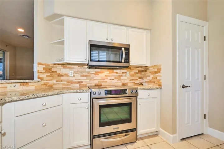 Kitchen with stainless steel appliances, open shelves, light tile patterned flooring, white cabinetry, and backsplash