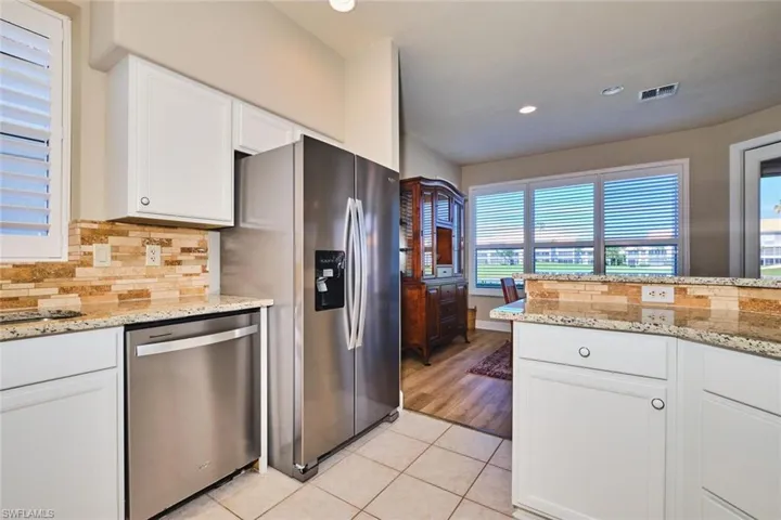 Kitchen featuring appliances with stainless steel finishes, white cabinetry, light tile patterned floors, backsplash, and light stone countertops