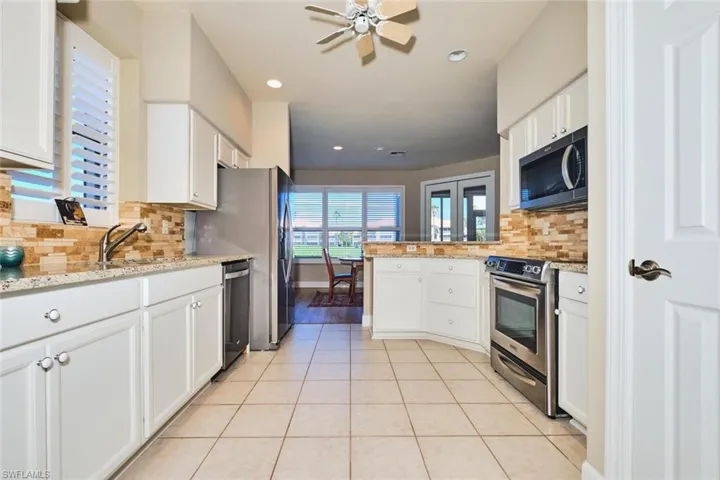 Kitchen with stainless steel appliances, ceiling fan, light tile patterned flooring, decorative backsplash, and a peninsula