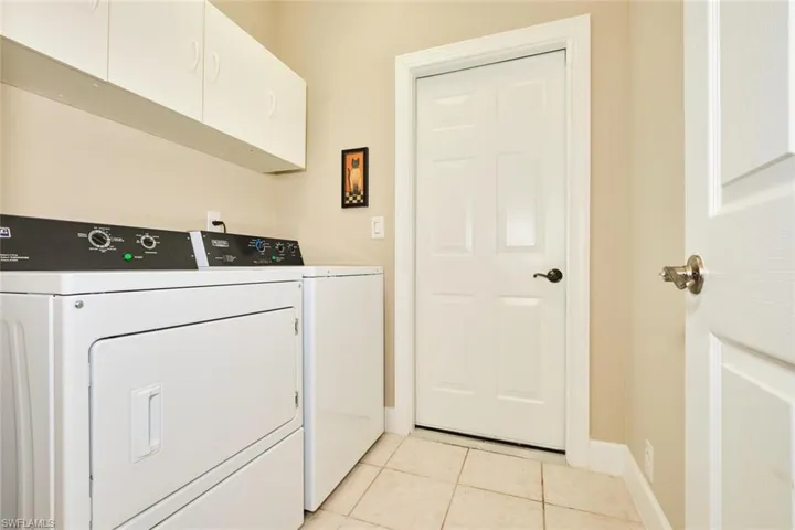 Laundry room featuring cabinet space, washer and dryer, light tile patterned floors, and baseboards