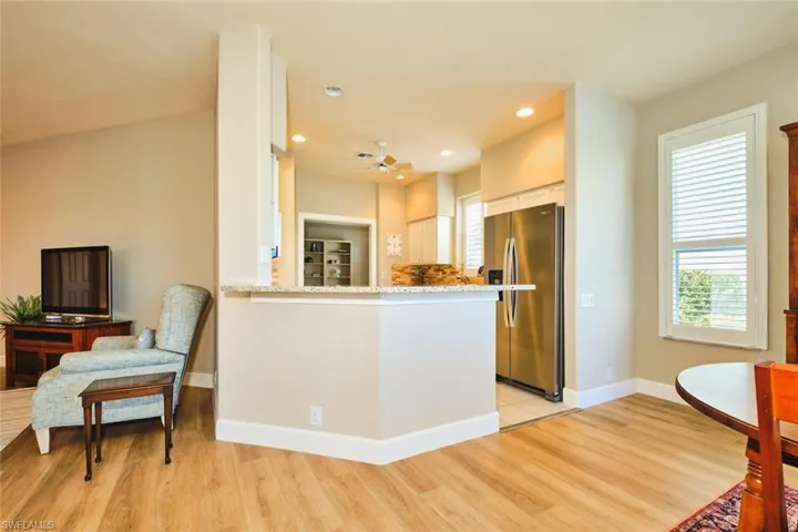 Kitchen featuring stainless steel refrigerator with ice dispenser, white cabinetry, light wood-type flooring, baseboards, and light stone counters