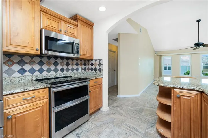Kitchen featuring stainless steel appliances, arched walkways, backsplash, open shelves, and light stone counters