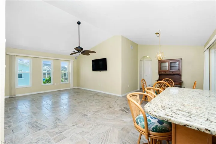 Dining area featuring stone tile floors, vaulted ceiling, ceiling fan, arched walkways, and a chandelier
