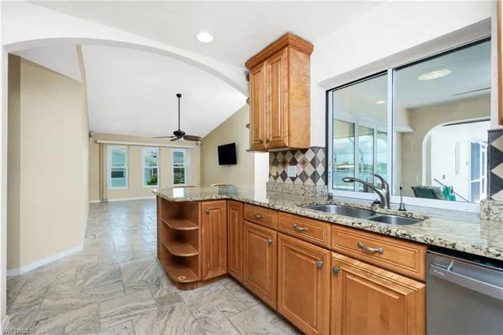 Kitchen with stainless steel dishwasher, vaulted ceiling, brown cabinetry, ceiling fan, and light stone countertops