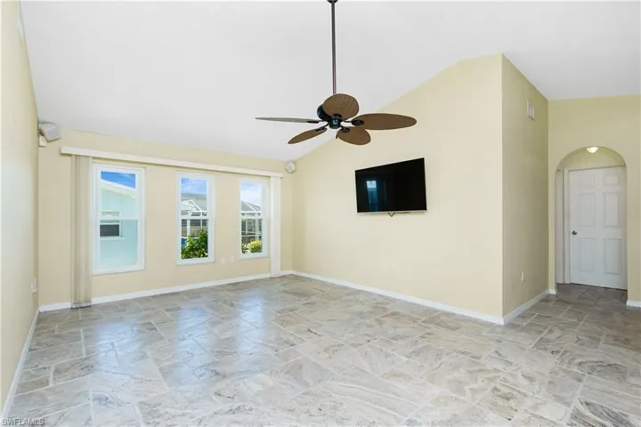 Empty room featuring stone tile flooring, vaulted ceiling, a ceiling fan, and arched walkways