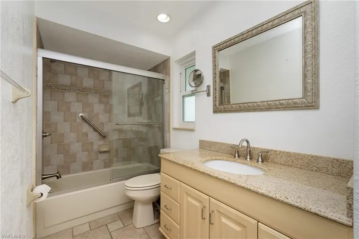 Full bathroom with vanity, shower / bath combination with glass door, stone finish floors, and recessed lighting