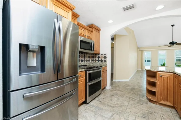 Kitchen with stainless steel appliances, arched walkways, tasteful backsplash, a ceiling fan, and light stone countertops