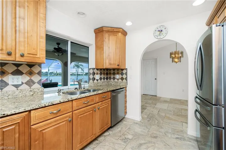 Kitchen featuring appliances with stainless steel finishes, stone tile floors, light stone counters, backsplash, and recessed lighting