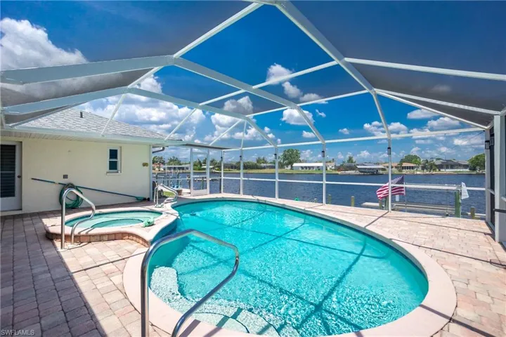 View of pool with a patio, a water view, a pool with connected hot tub, and a lanai