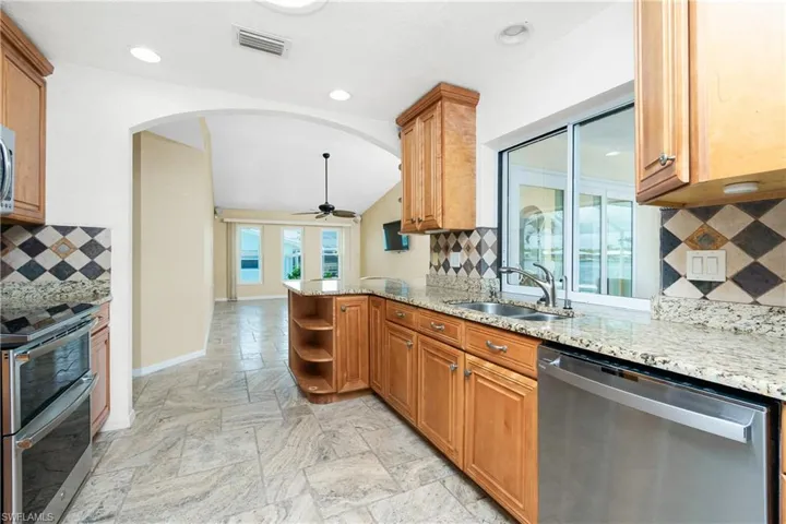 Kitchen featuring appliances with stainless steel finishes, arched walkways, tasteful backsplash, light stone countertops, and vaulted ceiling