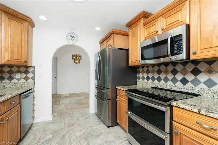Kitchen featuring stainless steel appliances, arched walkways, light stone finish floors, light stone counters, and backsplash
