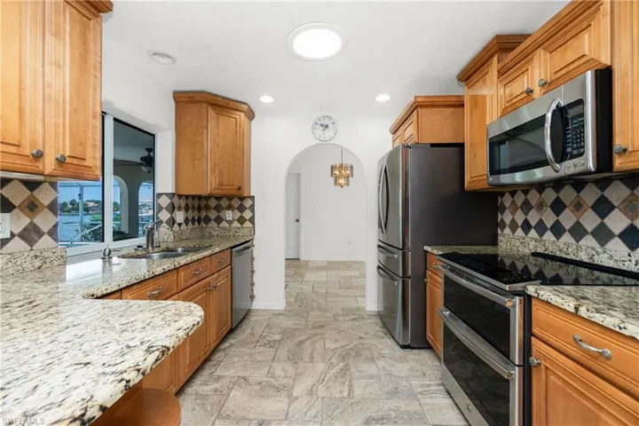 Kitchen featuring appliances with stainless steel finishes, stone tile floors, arched walkways, light stone countertops, and backsplash