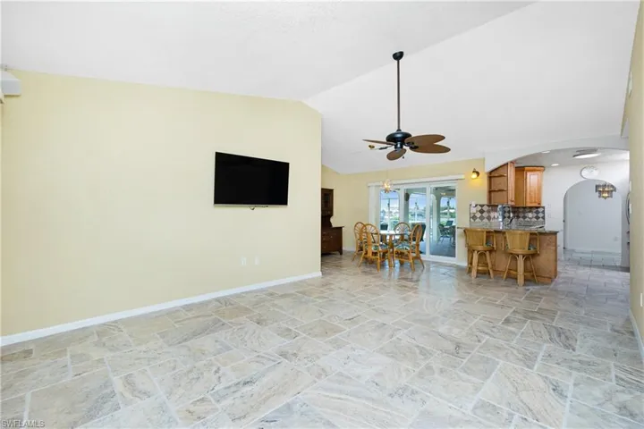 Living area with light stone finish flooring, arched walkways, ceiling fan, lofted ceiling, and a chandelier