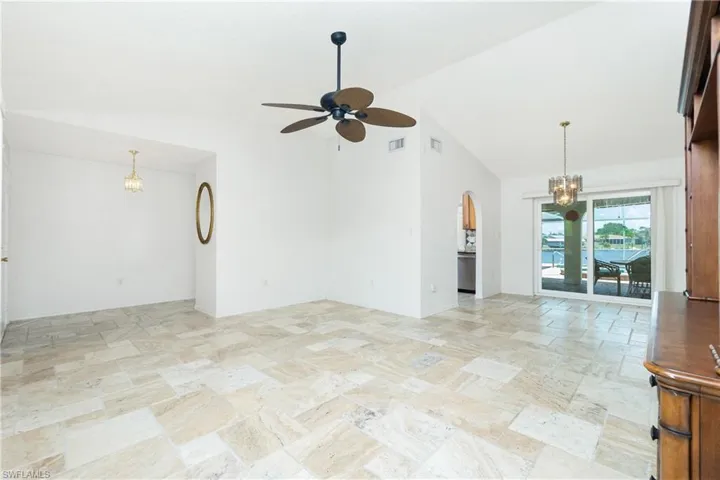 Unfurnished room with a chandelier, stone tile floors, a ceiling fan, arched walkways, and high vaulted ceiling
